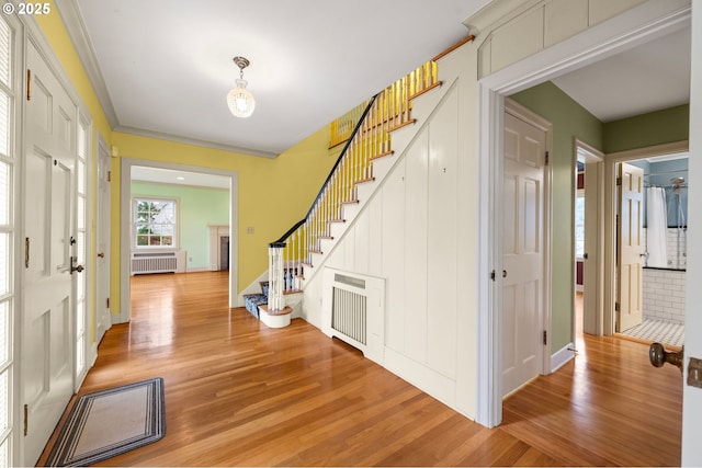 foyer with light wood finished floors, stairway, a fireplace, and radiator