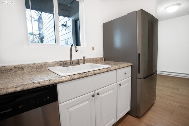 kitchen with a sink, white cabinetry, stainless steel appliances, light wood finished floors, and baseboard heating