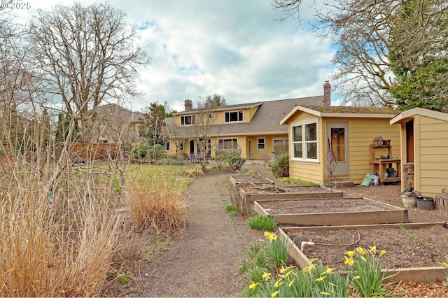 rear view of property featuring a vegetable garden, fence, roof with shingles, and a chimney