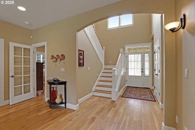 entrance foyer with light wood finished floors, baseboards, stairs, recessed lighting, and arched walkways