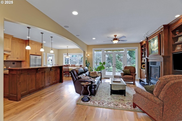 living room featuring a glass covered fireplace, recessed lighting, french doors, arched walkways, and light wood-style floors