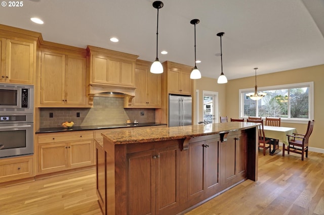 kitchen with light wood-type flooring, a center island, dark stone counters, appliances with stainless steel finishes, and decorative backsplash