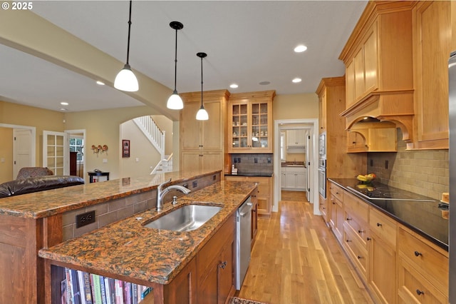 kitchen featuring a sink, black electric stovetop, a center island with sink, light wood-style flooring, and stainless steel dishwasher