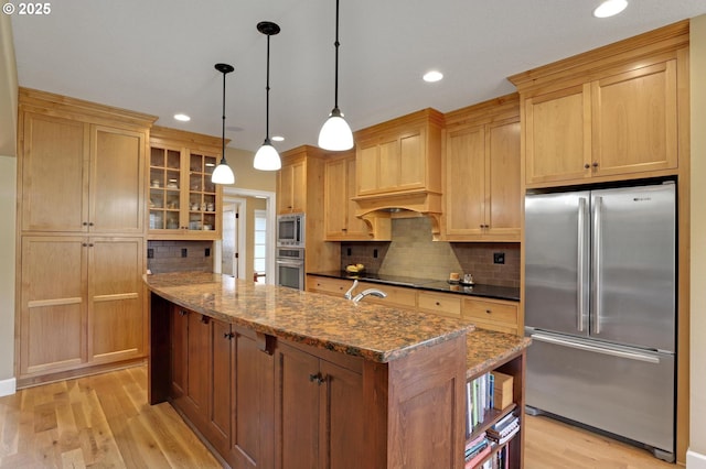 kitchen with light wood finished floors, stainless steel appliances, glass insert cabinets, backsplash, and a center island