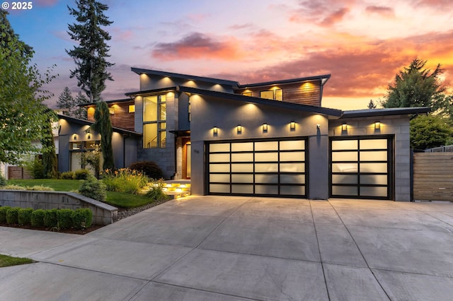 contemporary house featuring a garage, stucco siding, stone siding, and driveway