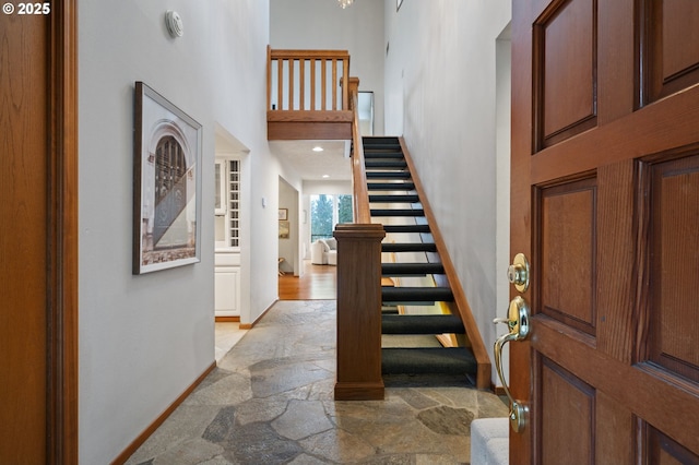 foyer with stairs, a high ceiling, stone tile flooring, and baseboards