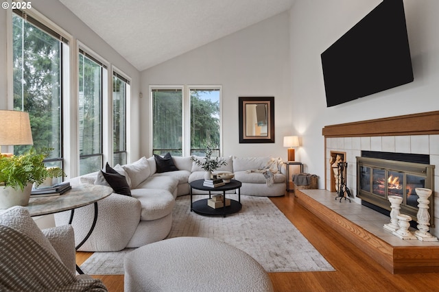 living area featuring light wood-style floors, a tile fireplace, and high vaulted ceiling