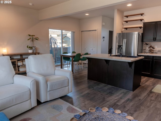 kitchen featuring a breakfast bar, sink, stainless steel fridge with ice dispenser, dark hardwood / wood-style floors, and a kitchen island with sink