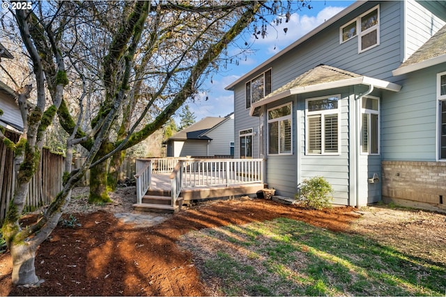 rear view of house featuring a deck, a shingled roof, and fence