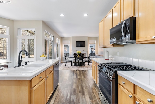 kitchen with black microwave, tile countertops, a sink, and range with gas stovetop