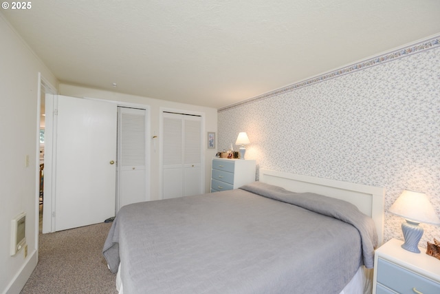 carpeted bedroom with two closets, wallpapered walls, and ornamental molding