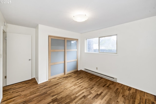 unfurnished bedroom featuring a closet, baseboard heating, and wood finished floors