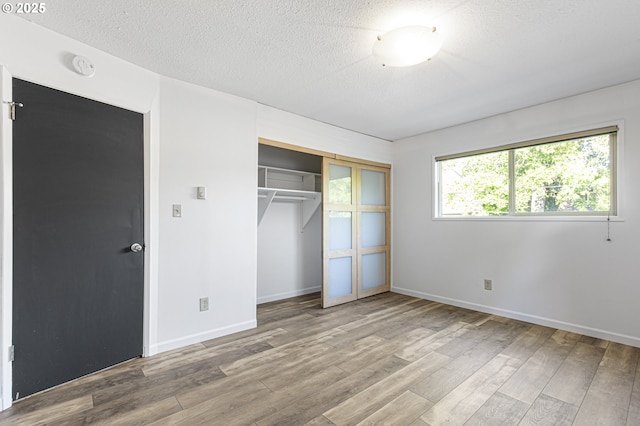 unfurnished bedroom featuring a closet, baseboards, a textured ceiling, and wood finished floors