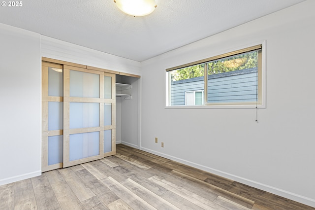 unfurnished bedroom featuring a closet, a textured ceiling, baseboards, and wood finished floors