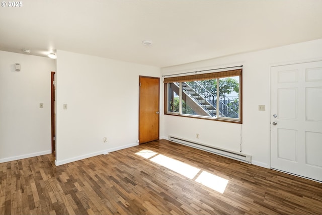 spare room with a baseboard heating unit, wood finished floors, and baseboards