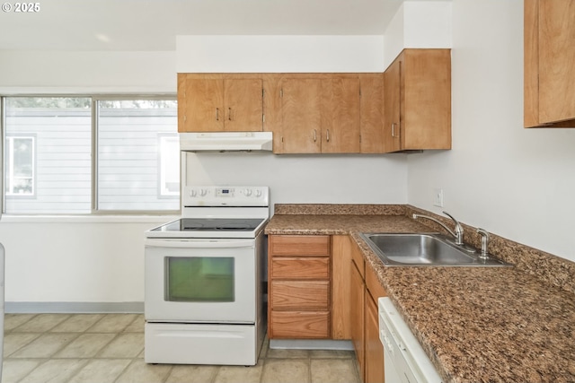 kitchen with dark countertops, under cabinet range hood, brown cabinets, white appliances, and a sink