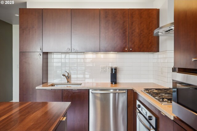 kitchen featuring stainless steel appliances, light stone countertops, a sink, and tasteful backsplash