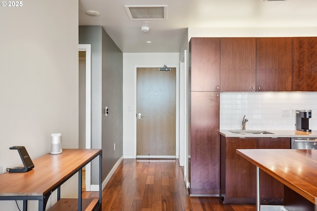 kitchen with tasteful backsplash, dark wood finished floors, brown cabinets, a sink, and baseboards