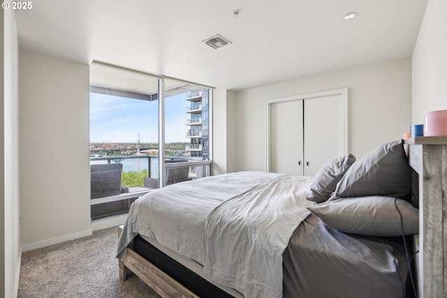 carpeted bedroom with baseboards, a water view, a closet, and visible vents
