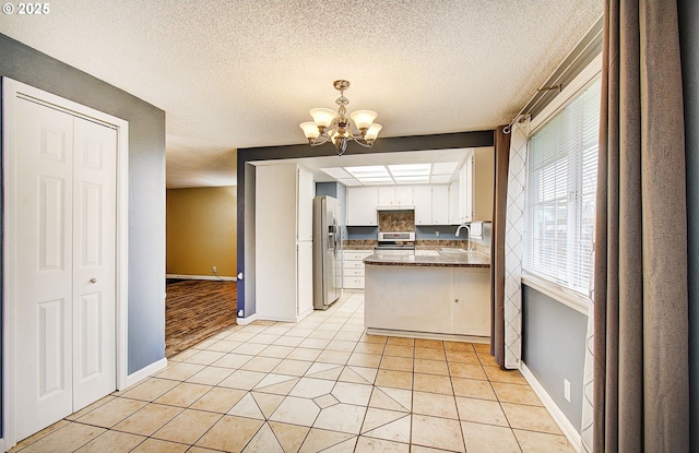 kitchen featuring kitchen peninsula, stainless steel appliances, a notable chandelier, white cabinetry, and light tile patterned flooring