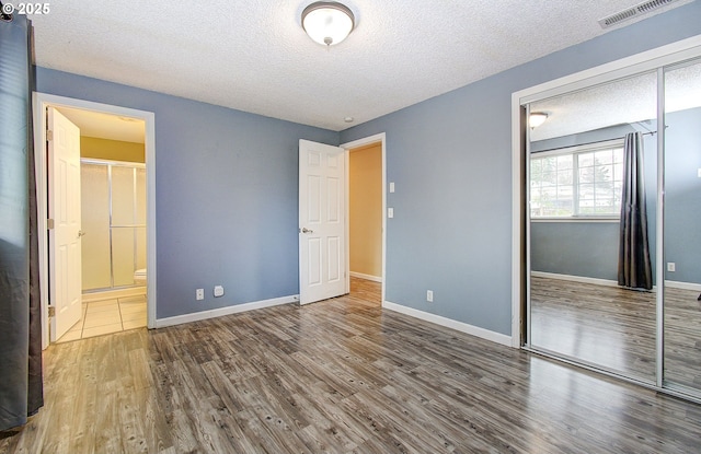 unfurnished bedroom featuring hardwood / wood-style flooring, a textured ceiling, connected bathroom, and a closet