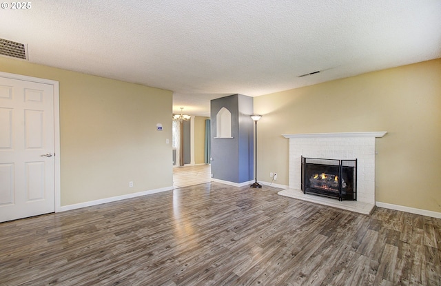 unfurnished living room featuring hardwood / wood-style flooring, a chandelier, a fireplace, and a textured ceiling