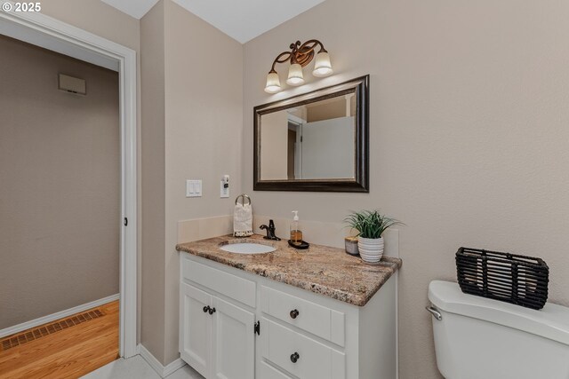 half bathroom featuring toilet, vanity, wood finished floors, and baseboards