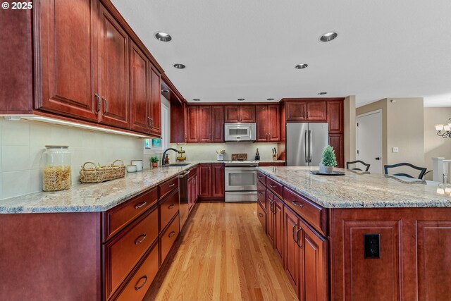 kitchen featuring appliances with stainless steel finishes, a sink, light wood-style flooring, light stone countertops, and recessed lighting