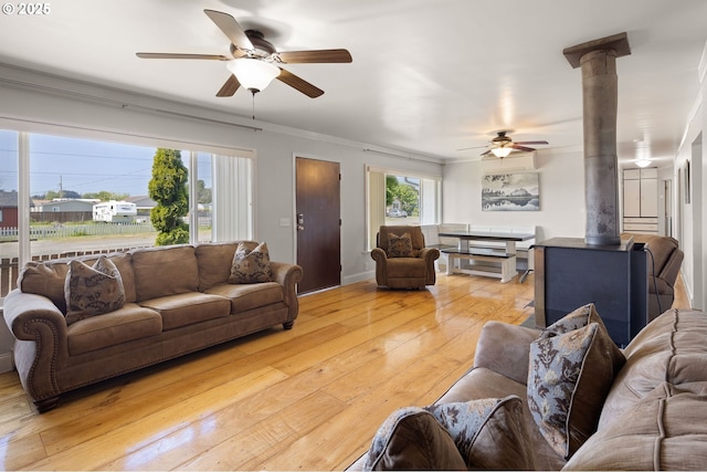 living room with a ceiling fan, ornamental molding, a wood stove, and light wood-style floors