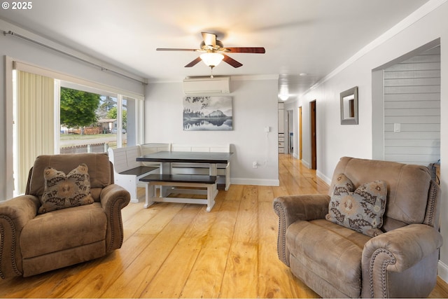 living area featuring light wood finished floors, a wall mounted air conditioner, a ceiling fan, baseboards, and ornamental molding