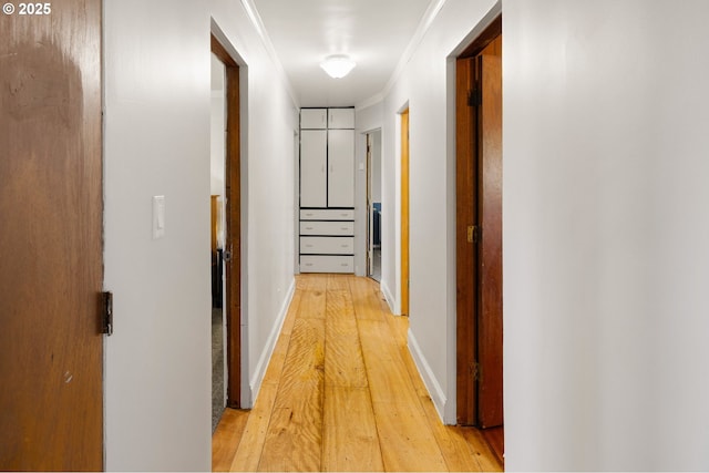 hallway with light wood-type flooring, ornamental molding, and baseboards