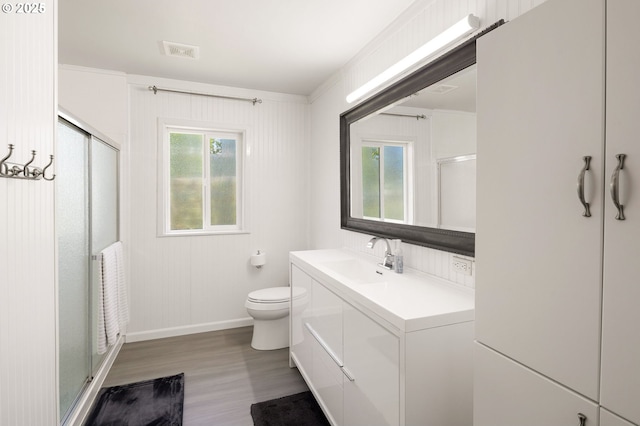 bathroom with vanity, toilet, wood finished floors, visible vents, and a stall shower
