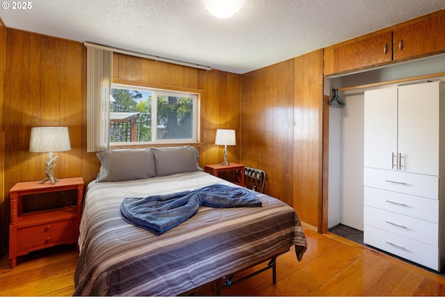 bedroom featuring light wood-style floors, wood walls, and a textured ceiling