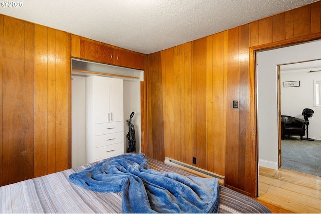 bedroom featuring wood walls, light wood-style flooring, a textured ceiling, and a baseboard heating unit