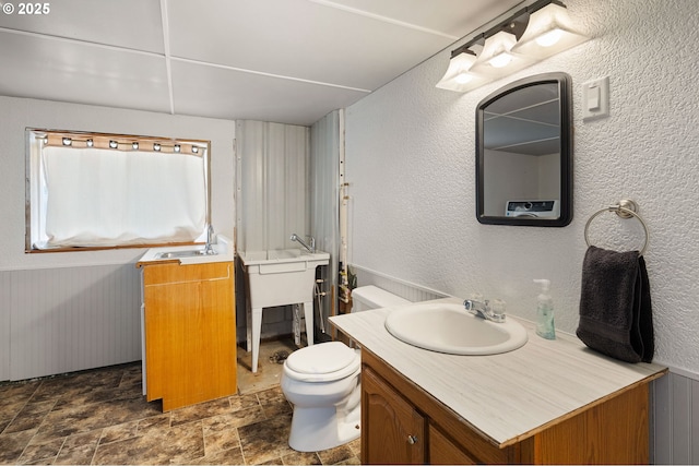 bathroom with vanity, stone finish flooring, a textured wall, and toilet