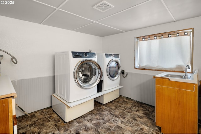 clothes washing area featuring cabinet space, a sink, separate washer and dryer, stone finish flooring, and visible vents