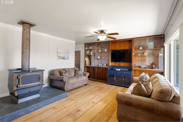 living area with wood-type flooring, a wood stove, ceiling fan, and crown molding