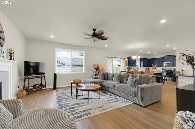 living room featuring ceiling fan with notable chandelier and light wood-type flooring