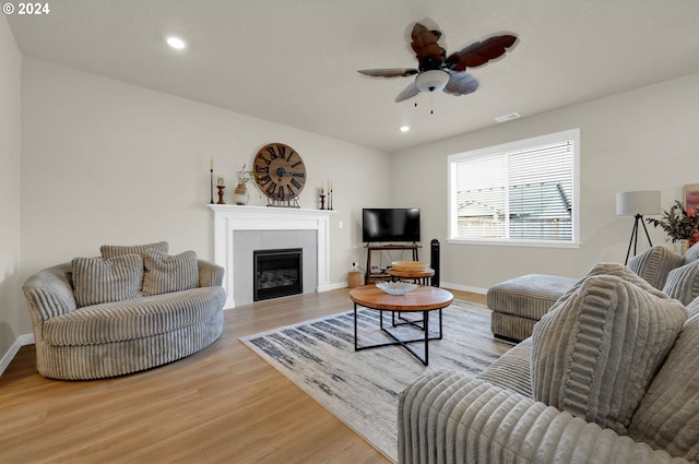 living room featuring a fireplace, ceiling fan, and light wood-type flooring