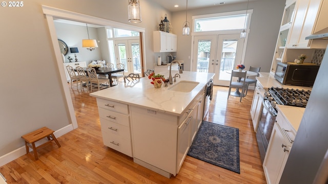 kitchen with french doors, white cabinetry, decorative light fixtures, and a center island with sink