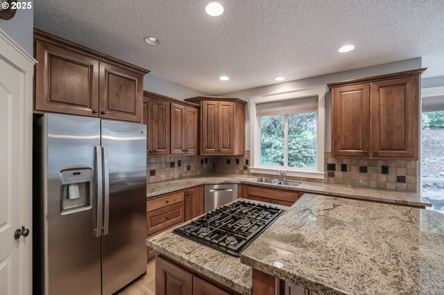 kitchen with light stone counters, stainless steel appliances, sink, and backsplash