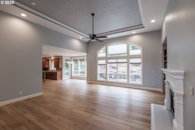 unfurnished living room with ceiling fan, a raised ceiling, a textured ceiling, and light wood-type flooring