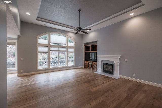 unfurnished living room featuring ceiling fan, wood-type flooring, a raised ceiling, and a wealth of natural light