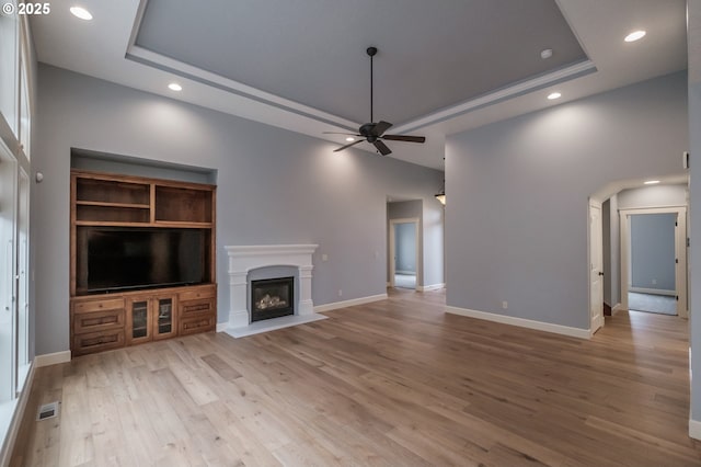 unfurnished living room featuring a high ceiling, a tray ceiling, ceiling fan, and light wood-type flooring