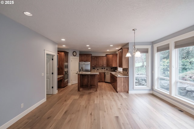 kitchen with pendant lighting, backsplash, stainless steel appliances, a kitchen island, and light wood-type flooring