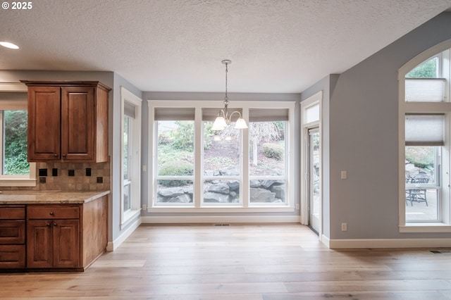 unfurnished dining area with a textured ceiling, an inviting chandelier, and light hardwood / wood-style flooring