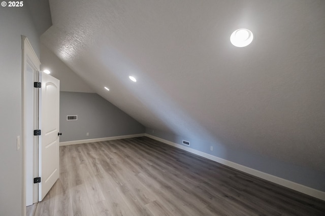 bonus room with lofted ceiling, light hardwood / wood-style floors, and a textured ceiling