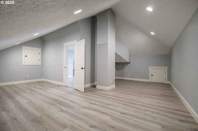 additional living space with lofted ceiling, a textured ceiling, and light hardwood / wood-style floors