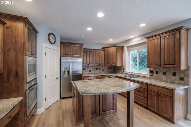 kitchen featuring appliances with stainless steel finishes, sink, a center island, light stone counters, and light hardwood / wood-style flooring