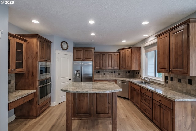 kitchen featuring a kitchen island, sink, light stone counters, stainless steel appliances, and light wood-type flooring